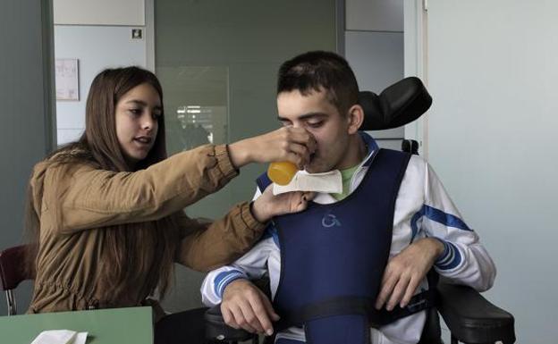 Marina ayuda a su hermano a beber un zumo de naranja. La chica ha dejado temporalmente los estudios para estar a su lado./MARTÍN BENET